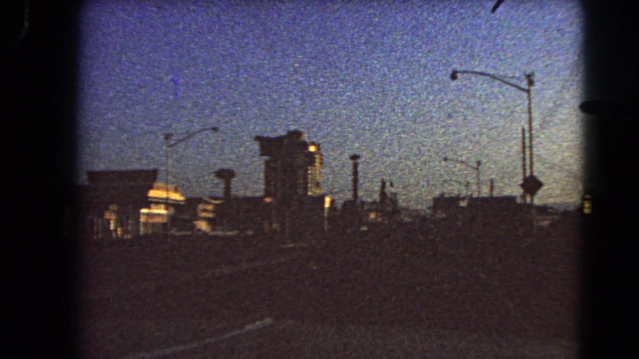 1966 Las Vegas dawn roadway view, with silhouetted buildings, streetlights, a tall structure, and a vertical roadside sign shape.