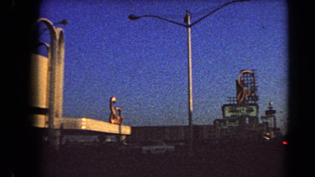 Dusk street view with tall lamps, a large illuminated sign, and dark traffic silhouettes.