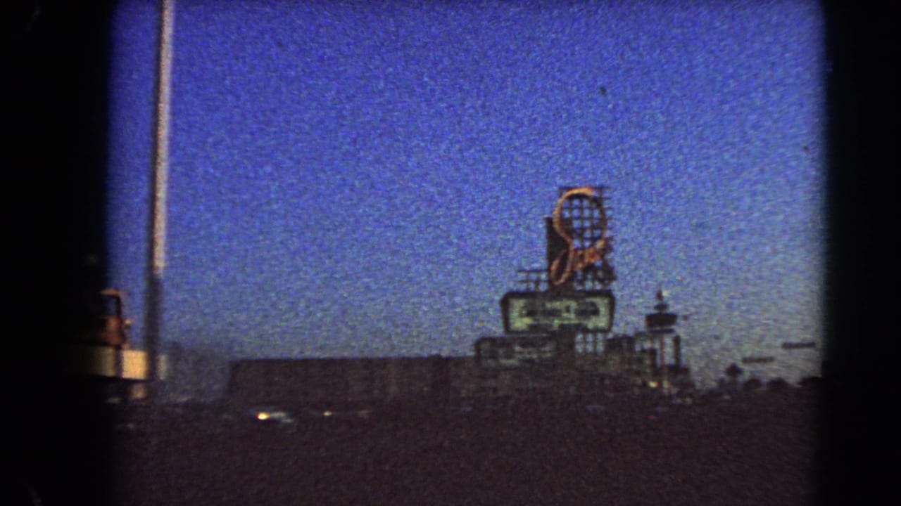 Large roadside sign and street lighting seen above a dark Las Vegas roadway at dusk.