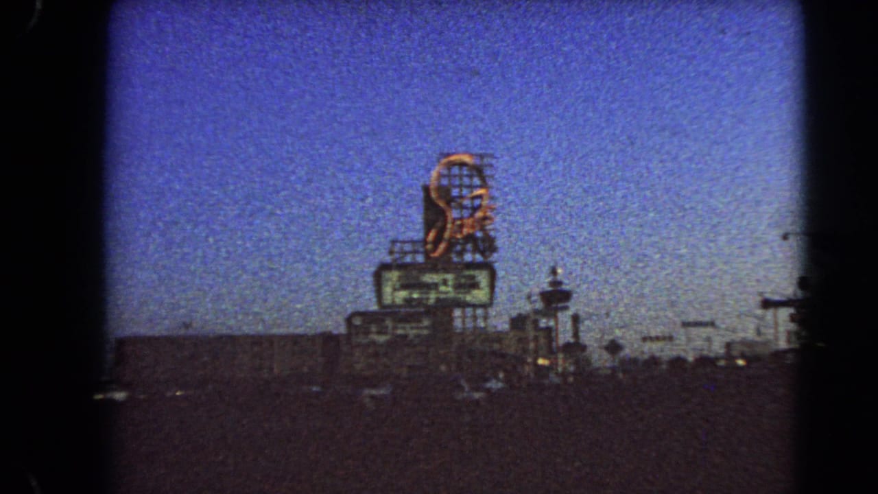 1966 Las Vegas street view with a tall lit sign, deep blue sky, dim traffic, and dark roadside structures.