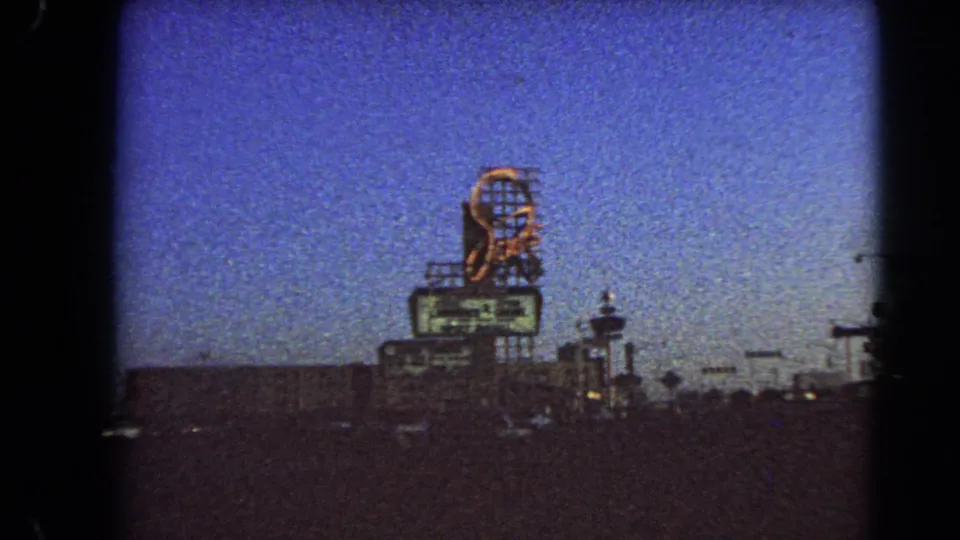 1966 Las Vegas street view with a tall lit sign, deep blue sky, dim traffic, and dark roadside structures.