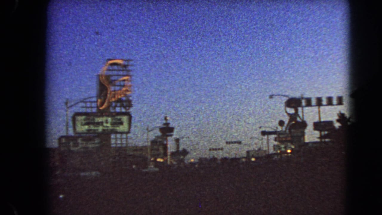 Late-frame 1966 Las Vegas driving view with a large sign, gate-like roadside lights, street poles, and shadowed traffic.