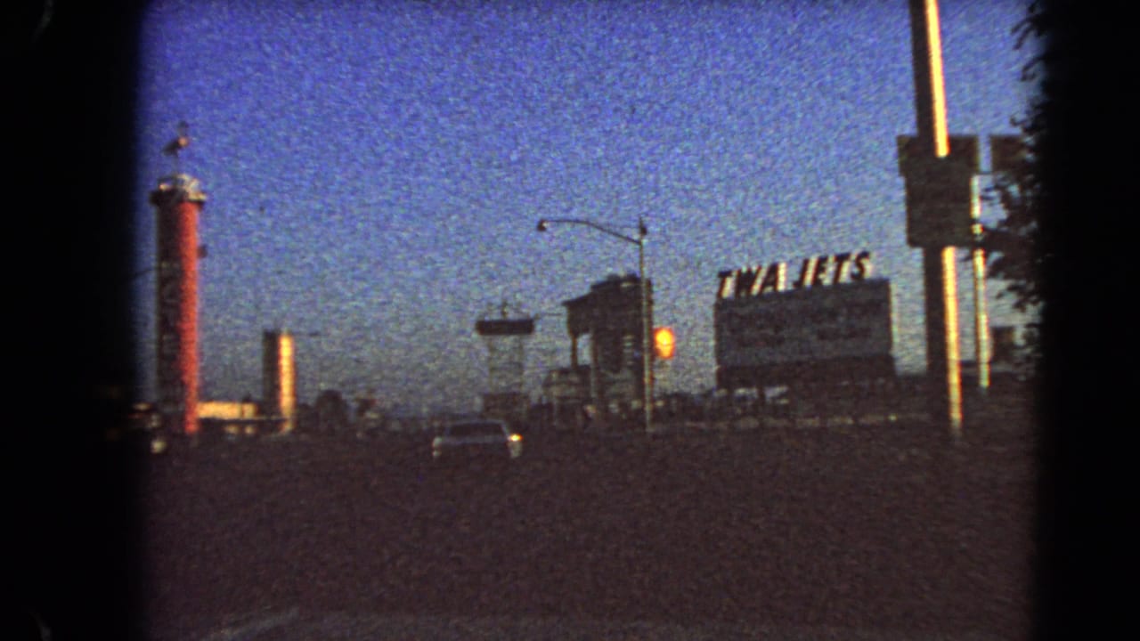 Roadside scene with TWA Jets billboard, Shell sign, red tower, car headlights, and streetlamp.