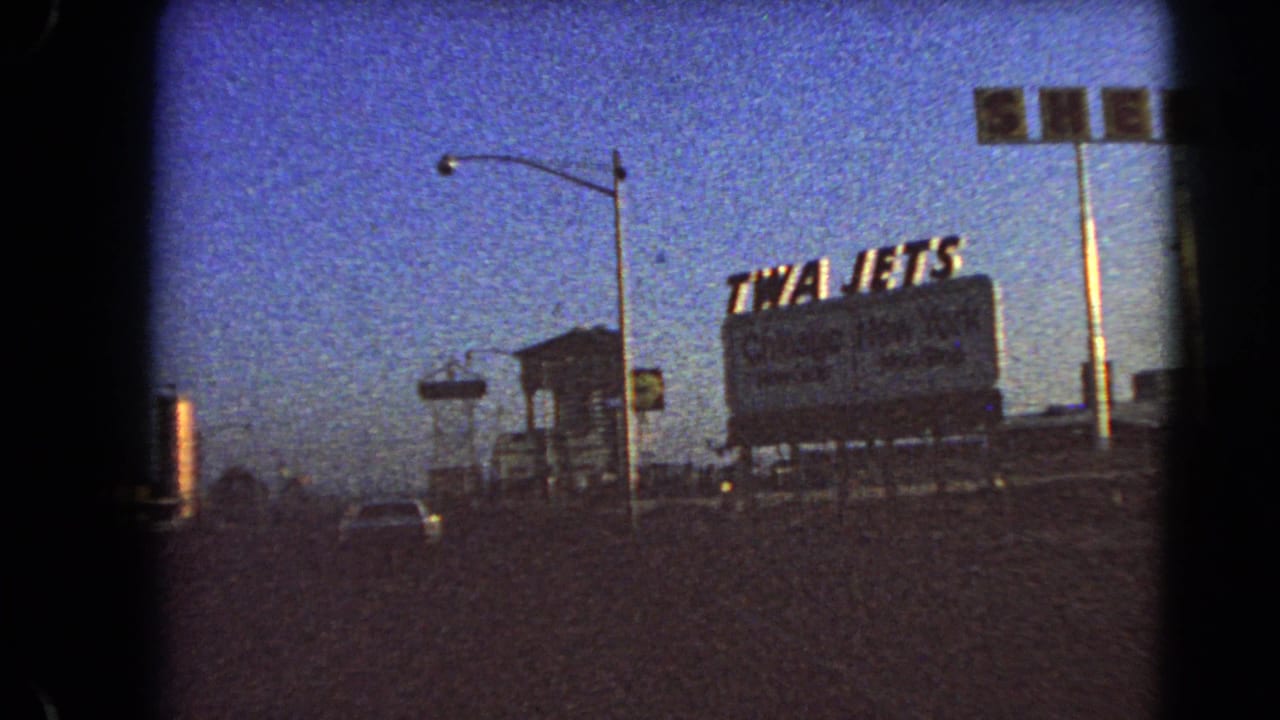 1966 Las Vegas drive-by view of a TWA Jets roadside billboard under a blue dusk sky, with a car, streetlights, and dark 8mm frame edges.