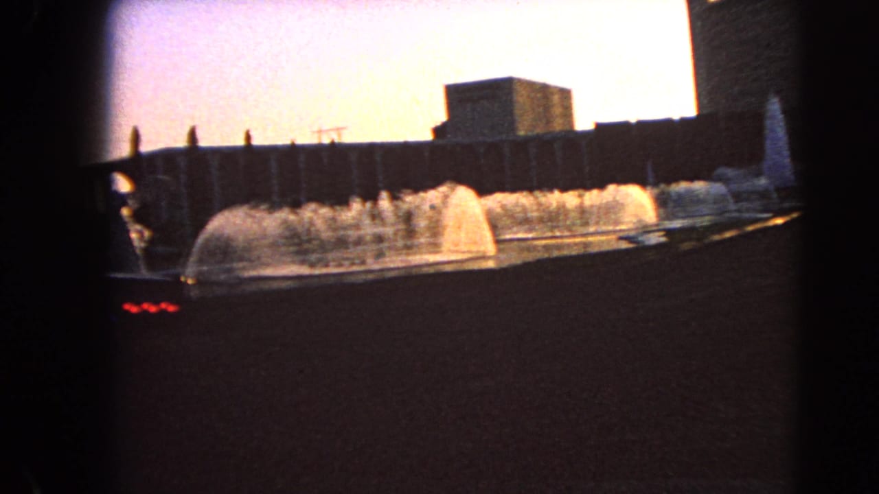 Wide fountain basin with arcing water jets and a blocky building behind it.