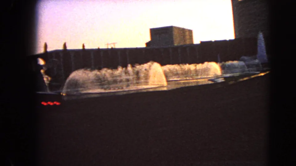 1966 Las Vegas 8mm frame with arcing fountain jets, a low dark foreground, and mid-century building forms in warm light.