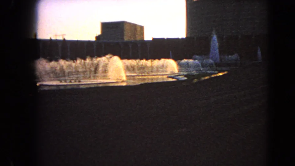1966 Las Vegas 8mm frame showing several fountain plumes and long building facades, with dark vignette and roadside foreground.