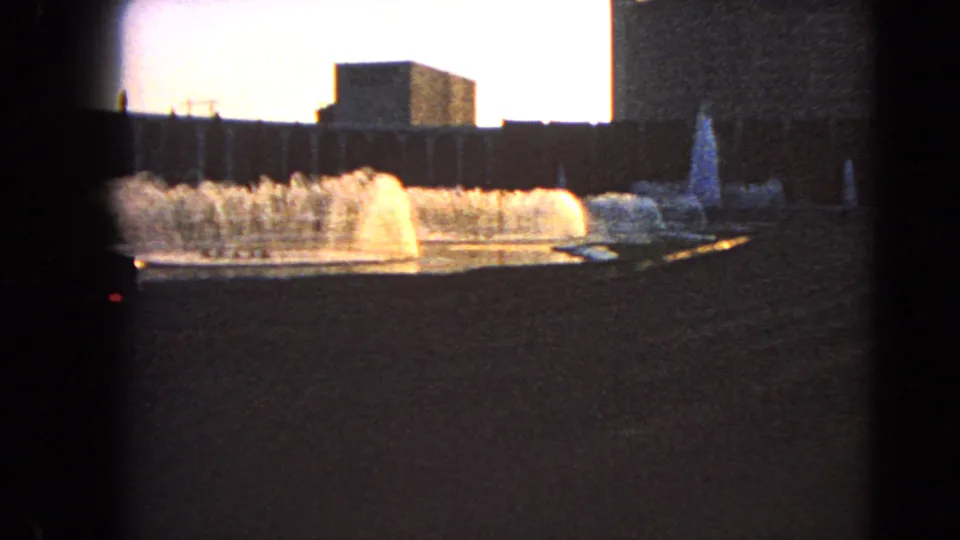 1966 Las Vegas home-movie frame showing fountain water jets and blocky buildings against an overexposed sky.
