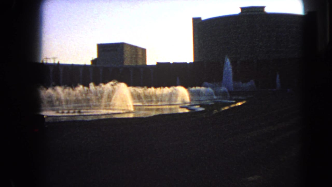 Vintage 8mm Las Vegas frame showing fountain spray across a plaza with modern building silhouettes.
