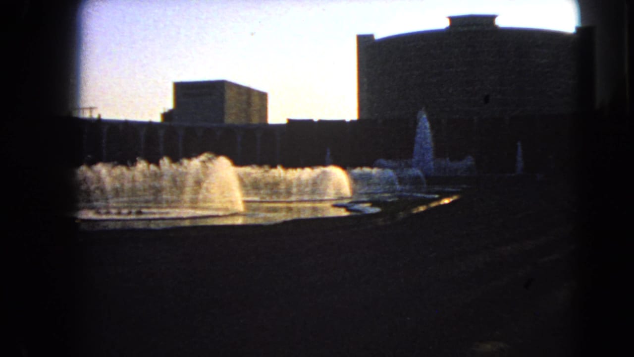 1966 Las Vegas 8mm frame showing a broad fountain basin and silhouetted modern building with strong edge vignetting.