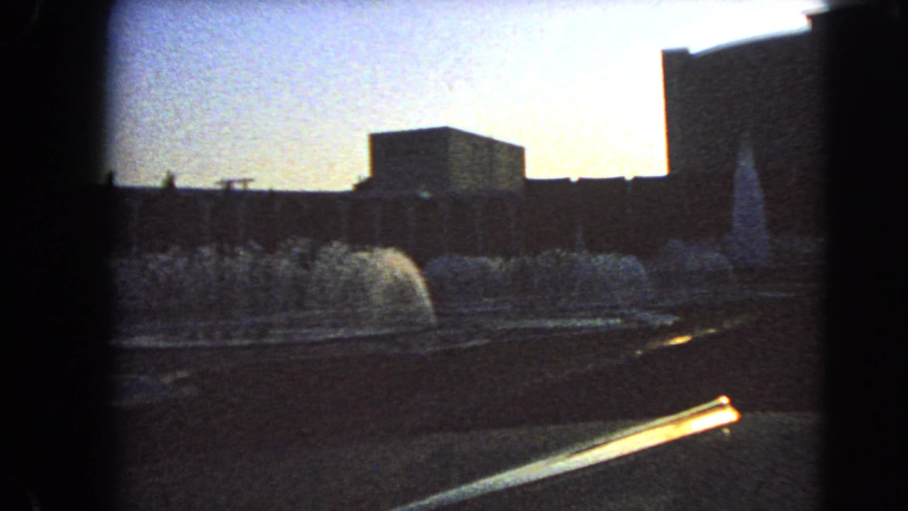 1966 Las Vegas home-movie frame showing fountains in a forecourt with silhouetted modern buildings beyond.
