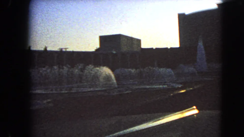1966 Las Vegas home-movie frame showing fountains in a forecourt with silhouetted modern buildings beyond.