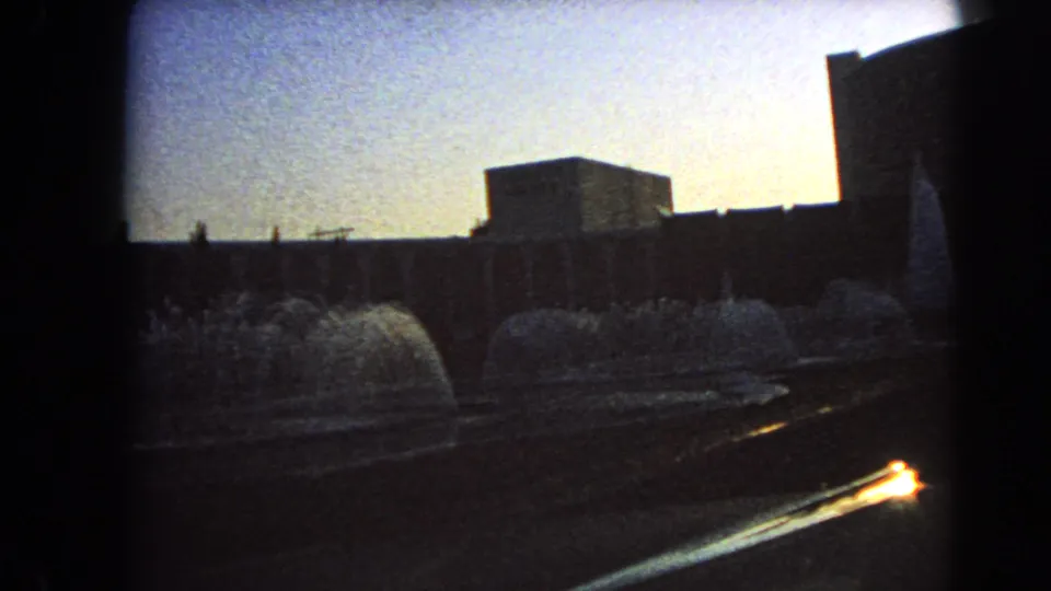 1966 Las Vegas 8mm frame with fountains, paved foreground, silhouetted buildings, and strong backlight.
