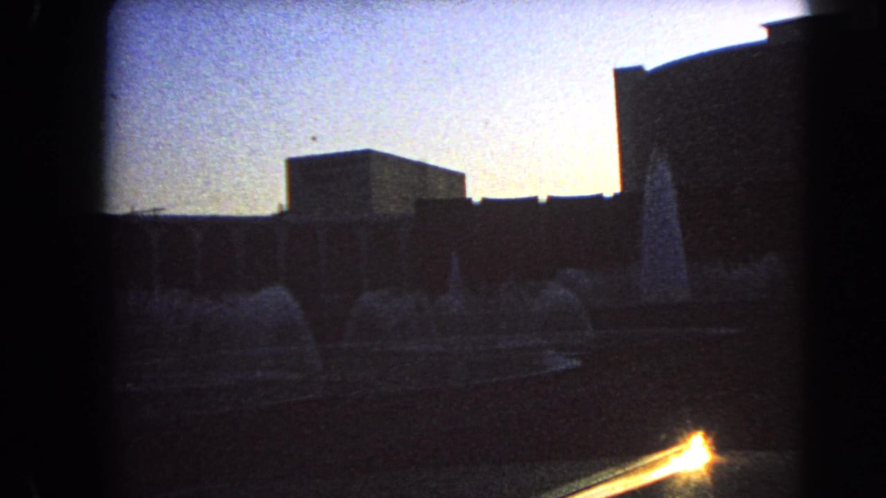1966 Las Vegas 8mm frame showing a dusk fountain courtyard with silhouetted modern buildings and low-light film grain.