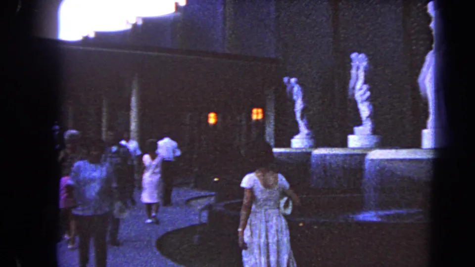 1966 Las Vegas courtyard scene with visitors in period clothing walking near fountain paving and classical-style statues.
