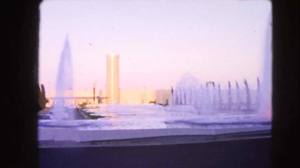 1966 Las Vegas home-movie frame showing a soft, overexposed fountain scene with water jets and a tall cylindrical tower in the distance.