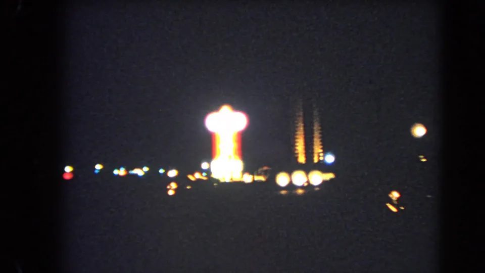 1966 Las Vegas Strip night footage showing a bright tower-like neon form, scattered lights, and grainy underexposed 8mm color.