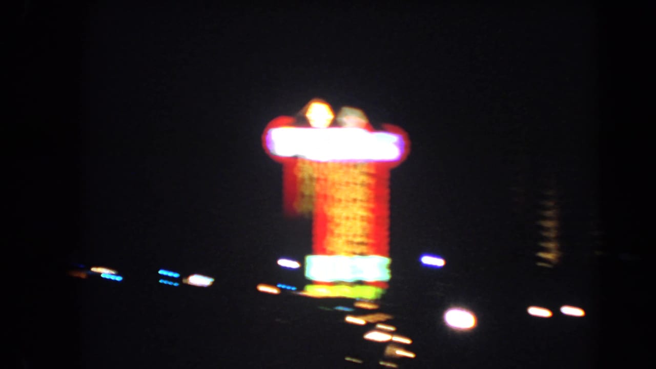 Close 8mm night view of a Las Vegas neon sign, with soft focus, bright bloom, and passing traffic lights.