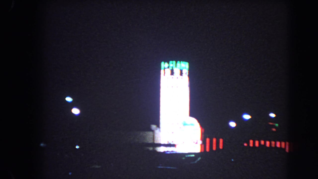 1966 Las Vegas night footage showing a bright hotel tower, red neon accents, streetlights, and dark open foreground.