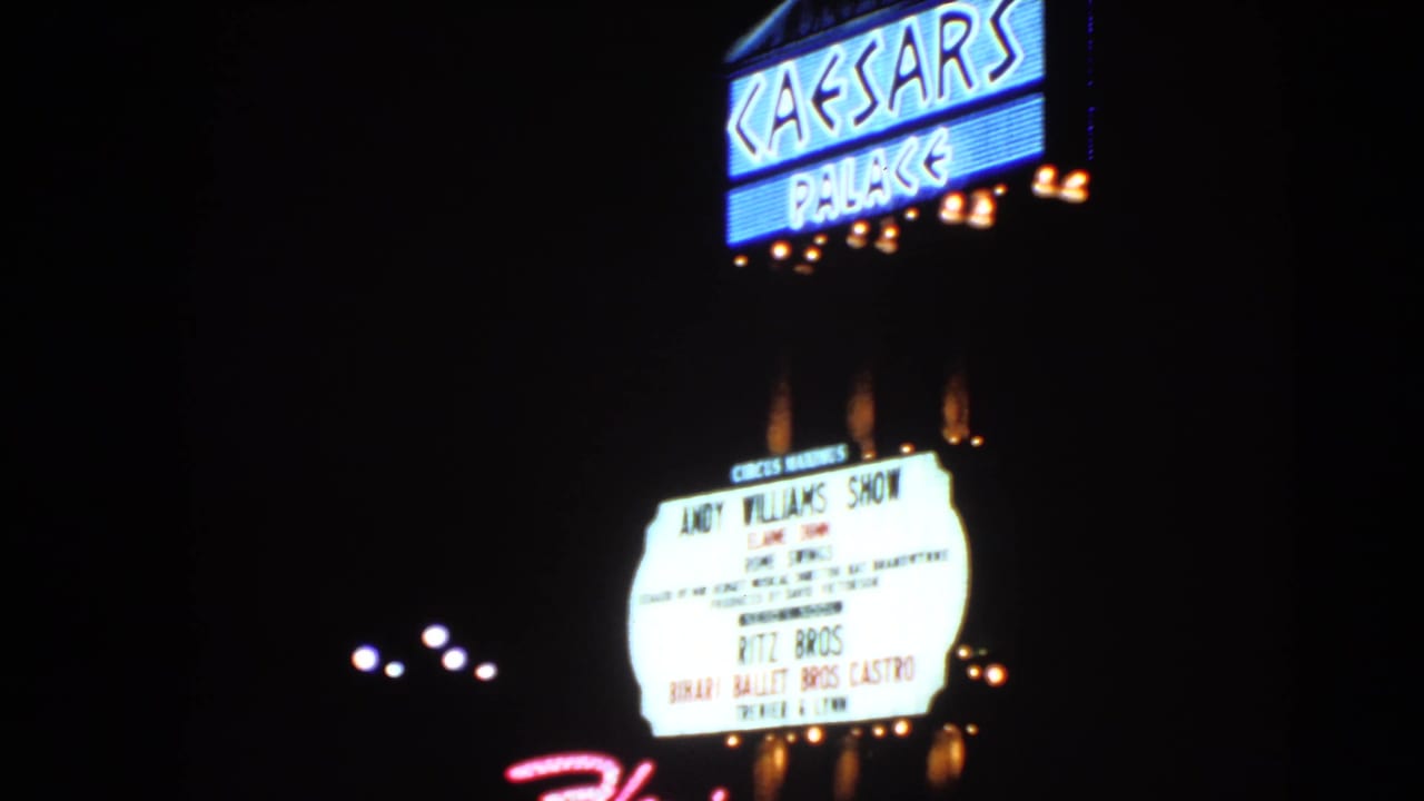 1966 Las Vegas night view of the Caesars Palace sign above a bright entertainment marquee, shot from a visitor perspective.