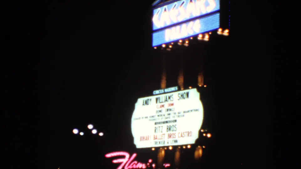 1966 Las Vegas home-movie frame of Caesars Palace neon and marquee signage, with soft focus and bright film exposure bloom.