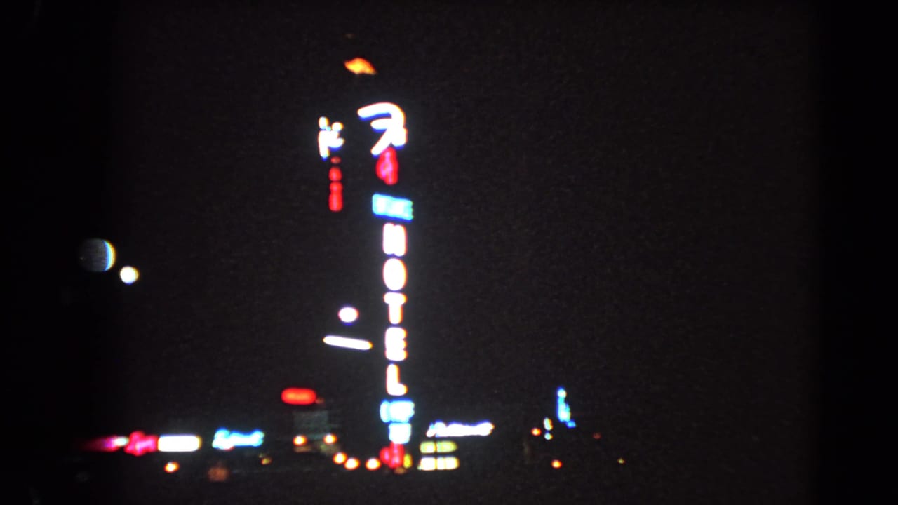 1966 Las Vegas night frame showing the hotel sign from a distance with small city lights and soft 8mm grain.