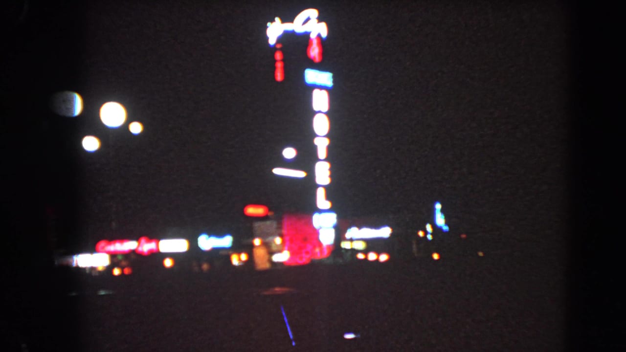 Blurred neon hotel sign and distant lights at night from a moving vehicle.