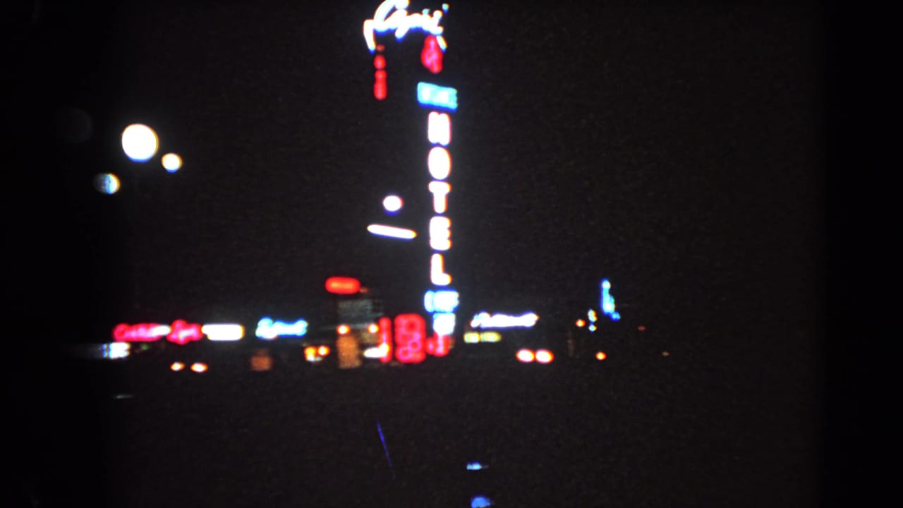 Nighttime neon hotel sign with surrounding city lights and dark foreground.