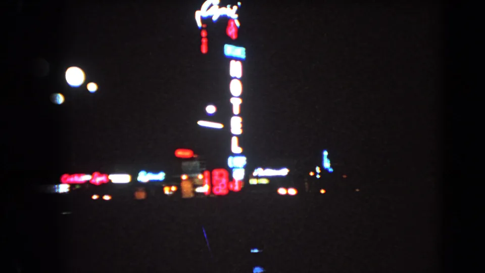 1966 Las Vegas footage shows a tall glowing hotel sign, nearby illuminated signs, streetlights, and heavy night-film grain.