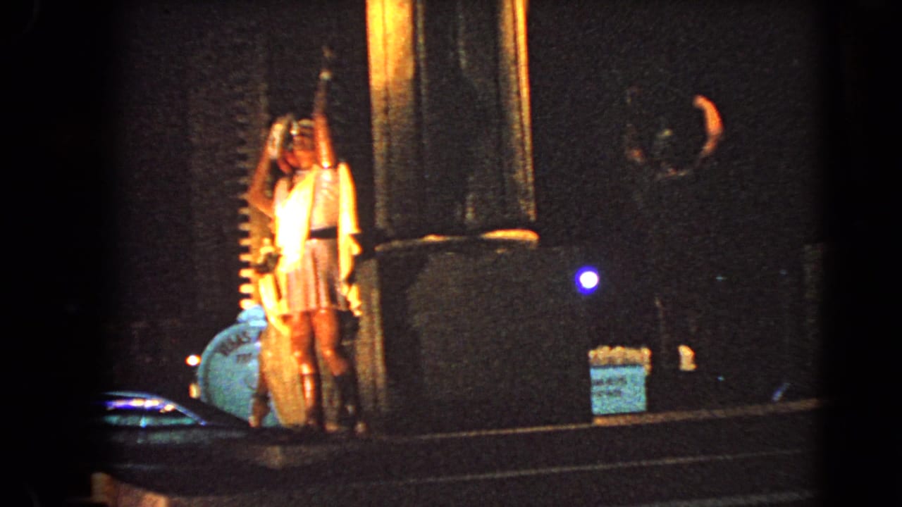 Illuminated male statues stand near tall columns in a dark nighttime setting.