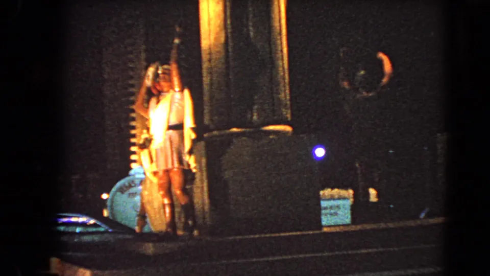 1966 Las Vegas home-movie frame showing lit male statues beside columns and a blue object at night.