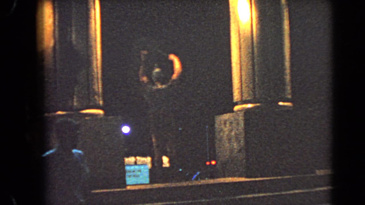 Dark nighttime display with columns, a small sign, and colored points of light.