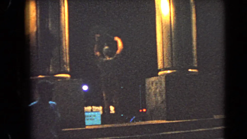 1966 Las Vegas night frame with columns, a small sign, and distant colored lights in a roadside scene.