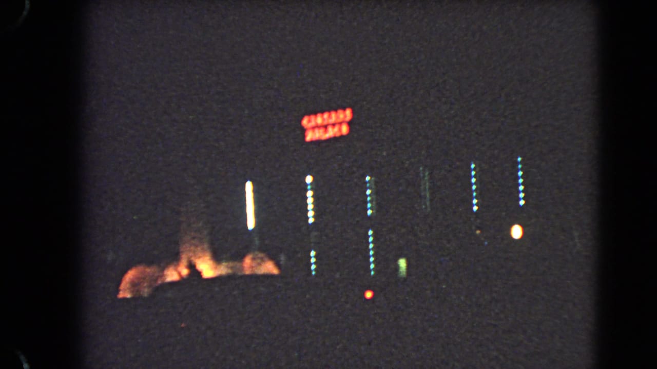 Red neon sign and rows of blue-white lights on a dark hotel exterior at night.