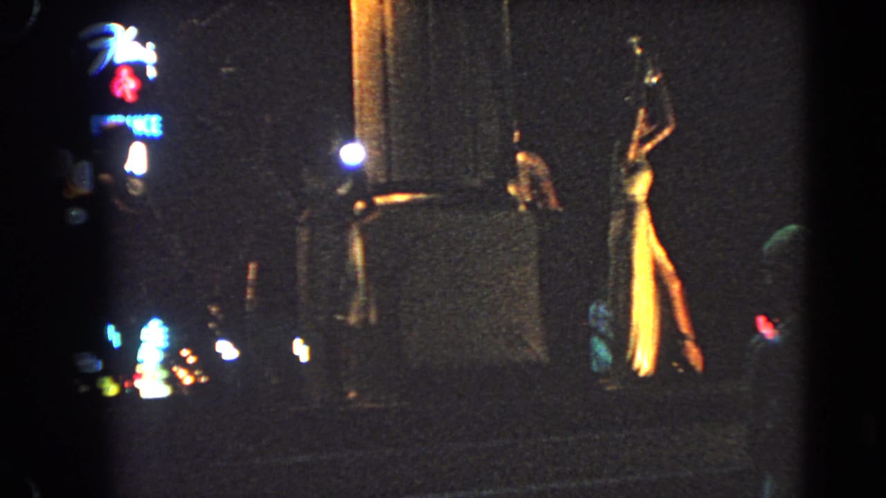 1966 Las Vegas street-level view showing neon signage, reflective pavement, and pedestrians near a lit hotel or casino entrance.