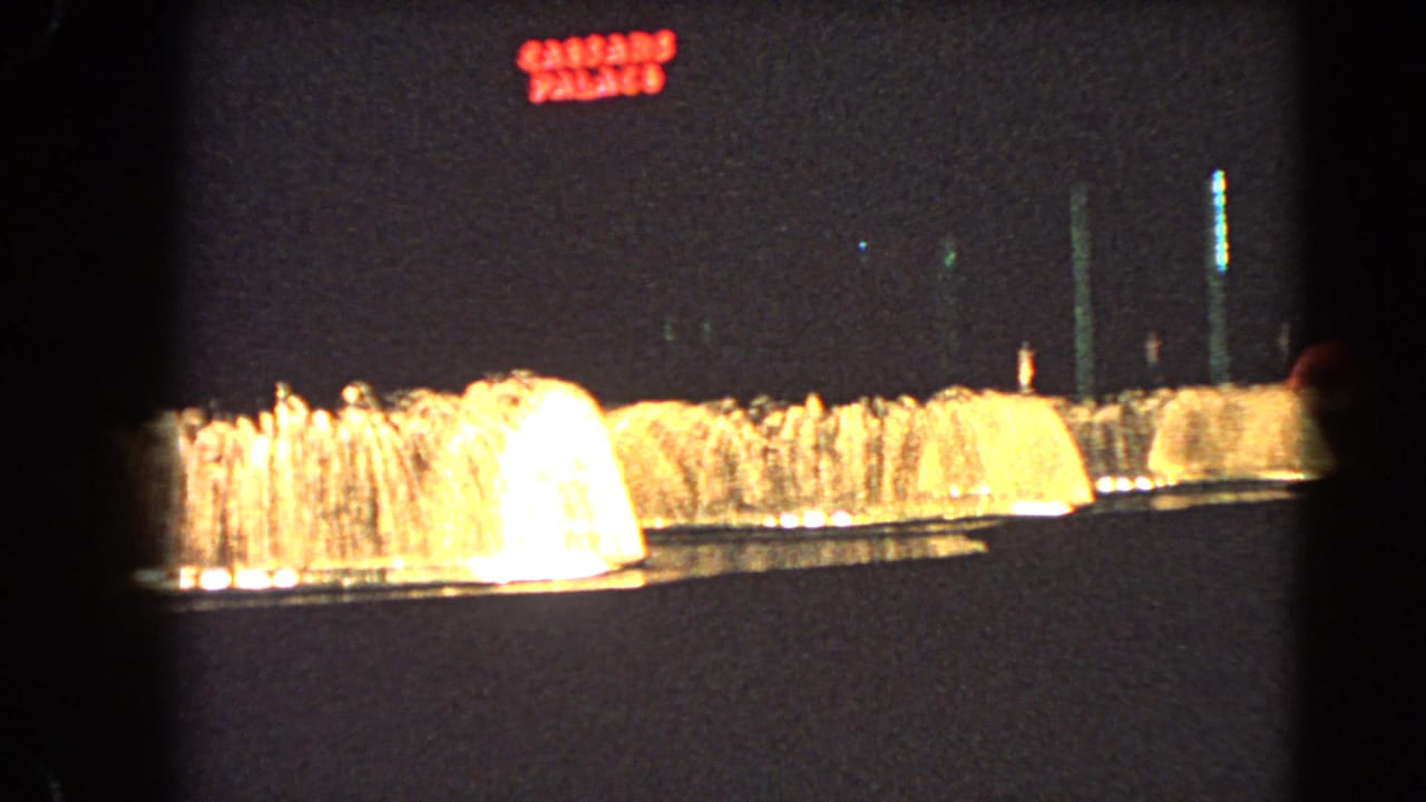 A wide night view shows warm-lit fountains with the red Caesar's Palace sign visible above in Las Vegas.
