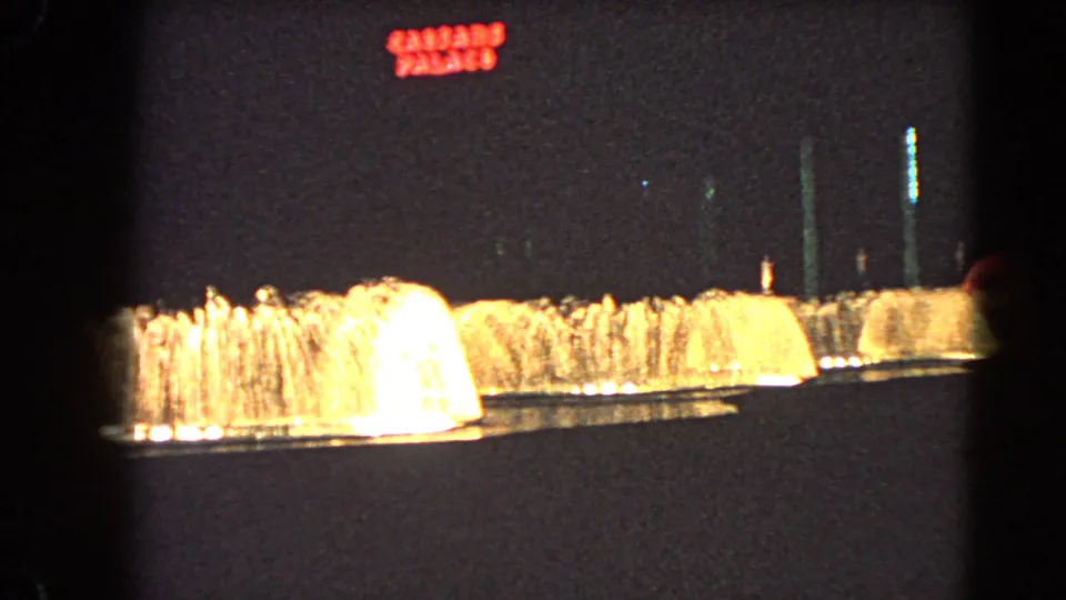 A wide night view shows warm-lit fountains with the red Caesar's Palace sign visible above in Las Vegas.