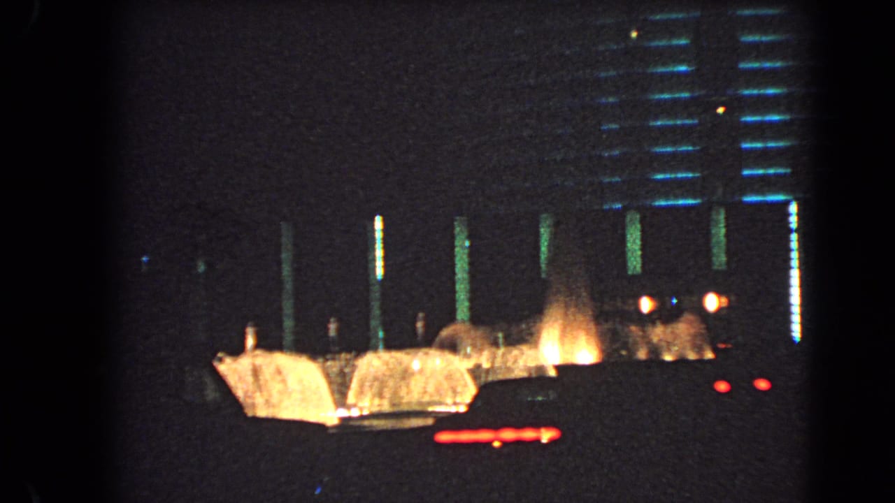 1966 Las Vegas home-movie frame showing a dark roadside view with illuminated building details, warm light, and red car taillights.