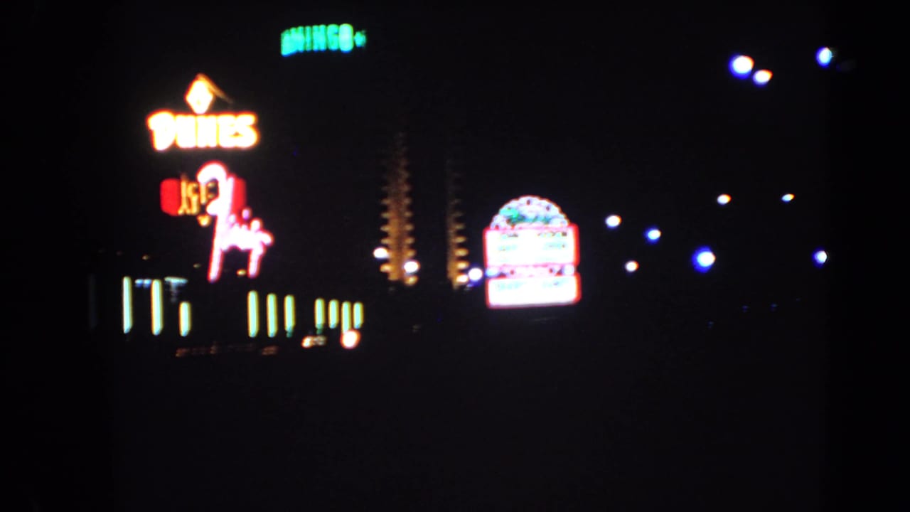 1966 Las Vegas frame with the Dunes sign, neon horse-and-rider figure, roadside lights, and another glowing marquee in the distance.