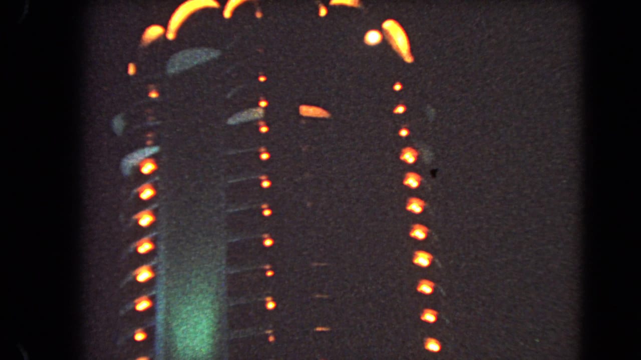 Tall illuminated facade with vertical orange lights and green glow at night.