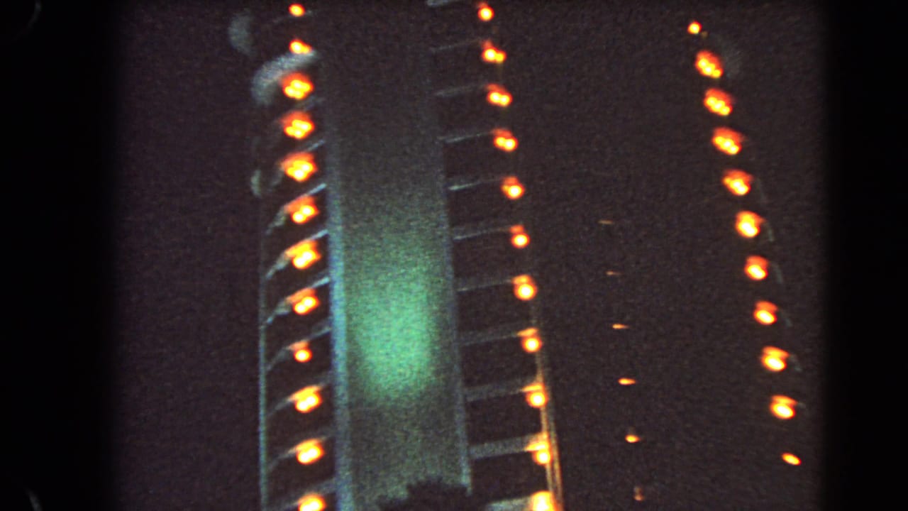 1966 Las Vegas night frame with a large illuminated exterior, vertical orange bulbs, green glow, and heavy 8mm grain.