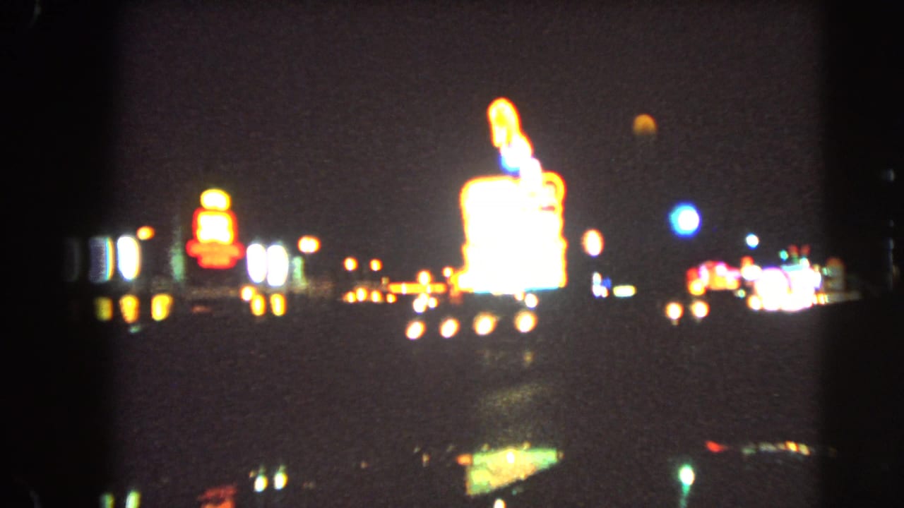 Blurred neon signs and car lights along a dark Las Vegas roadway at night.