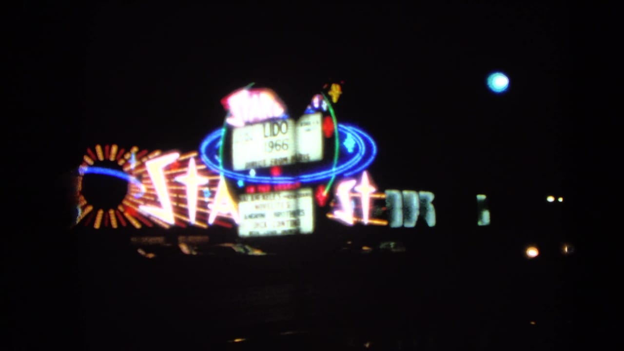 Stardust neon sign glowing beside other illuminated roadside signs at night.