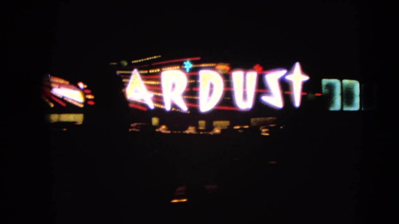 1966 Las Vegas night frame with a blurred Stardust neon sign glowing beside a dark roadway.