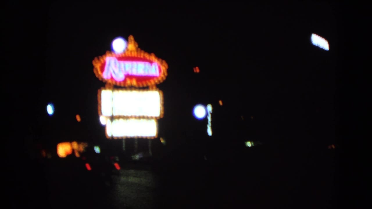 Riviera neon sign and bright marquee panels along a dark street.