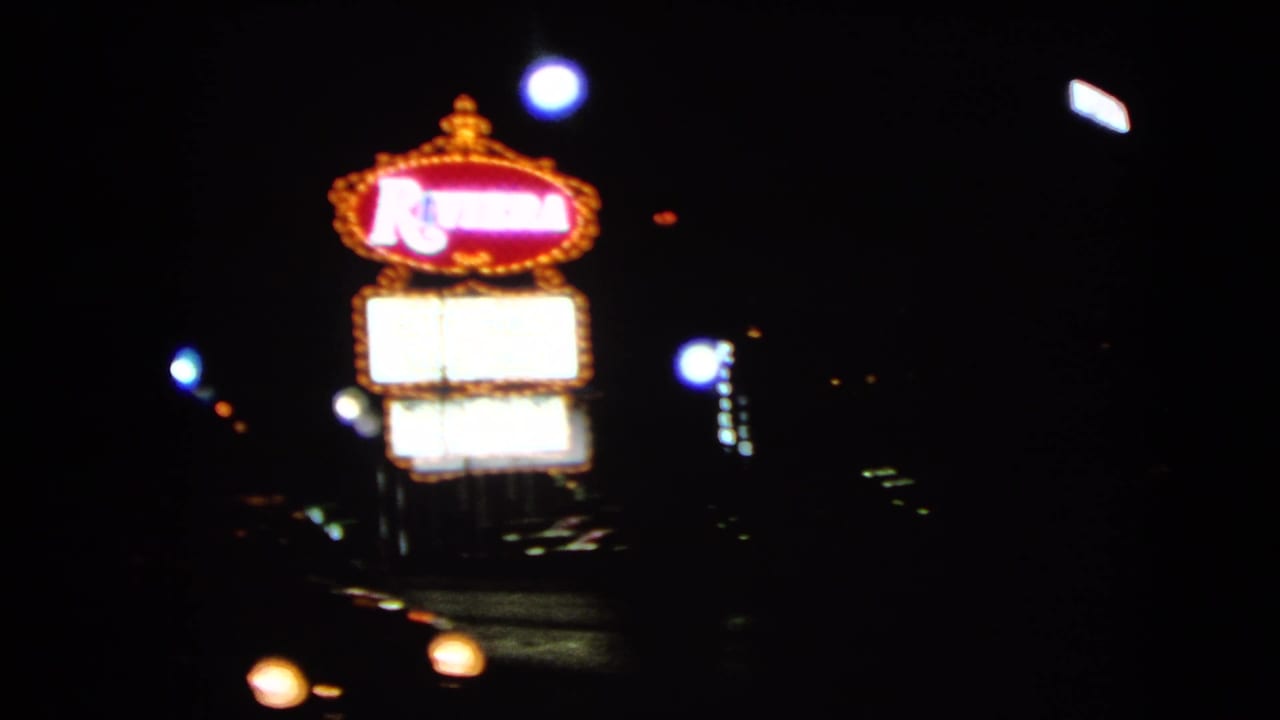 Moving 8mm view of the Riviera sign in Las Vegas, with headlights crossing the dark street below.