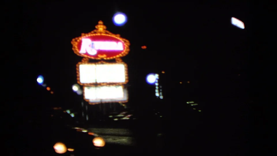 Moving 8mm view of the Riviera sign in Las Vegas, with headlights crossing the dark street below.