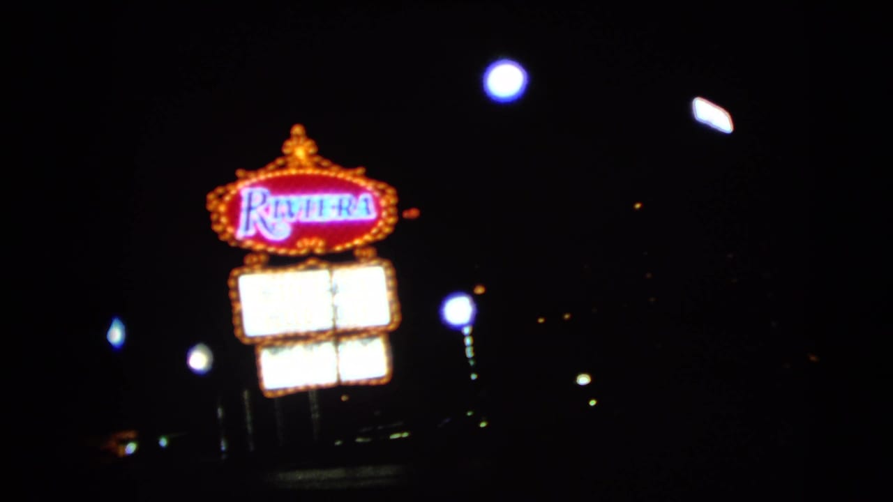 1966 Las Vegas night frame with the Riviera sign receding amid streetlights and blurred vehicle lights.