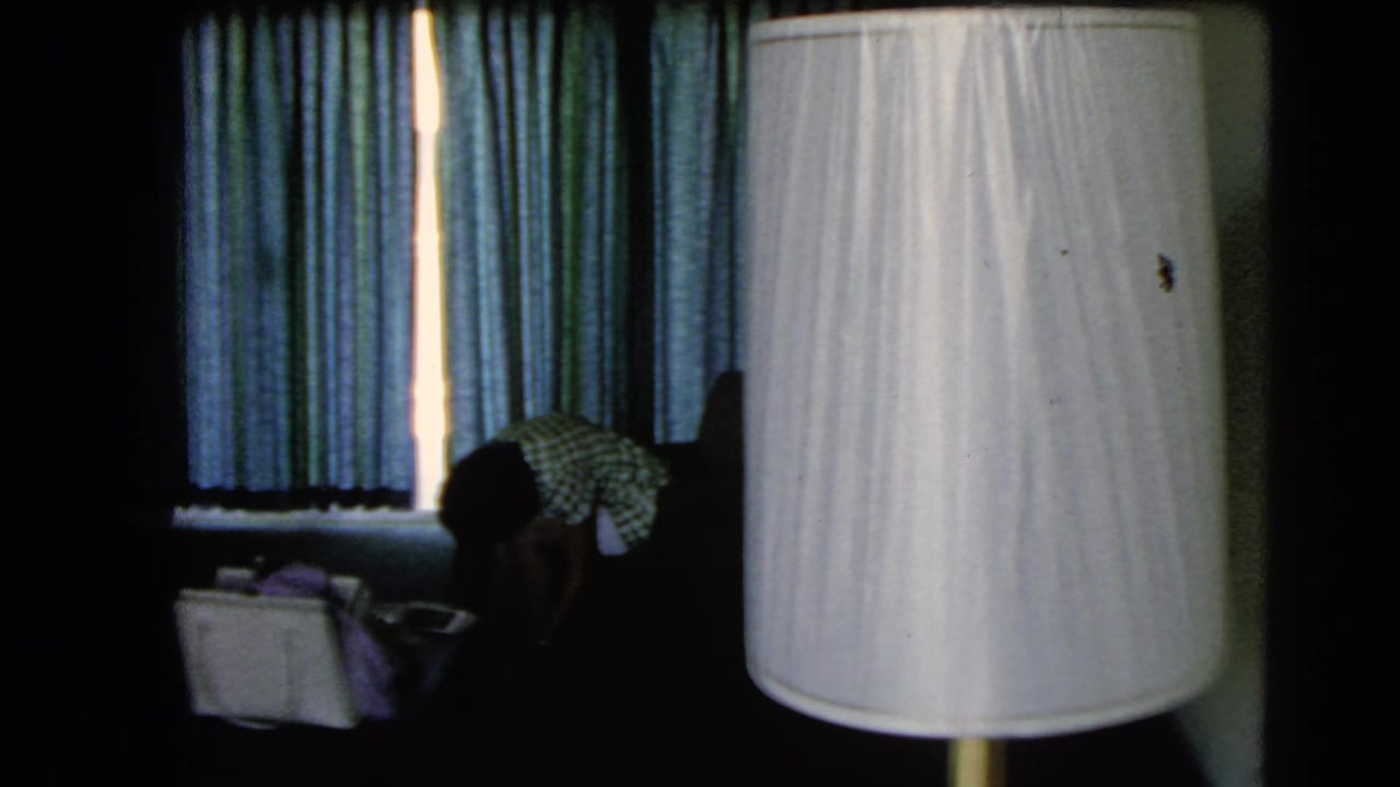 1966 Las Vegas home-movie frame showing a dim interior, curtains, a white lampshade, and a person partly visible near the window.