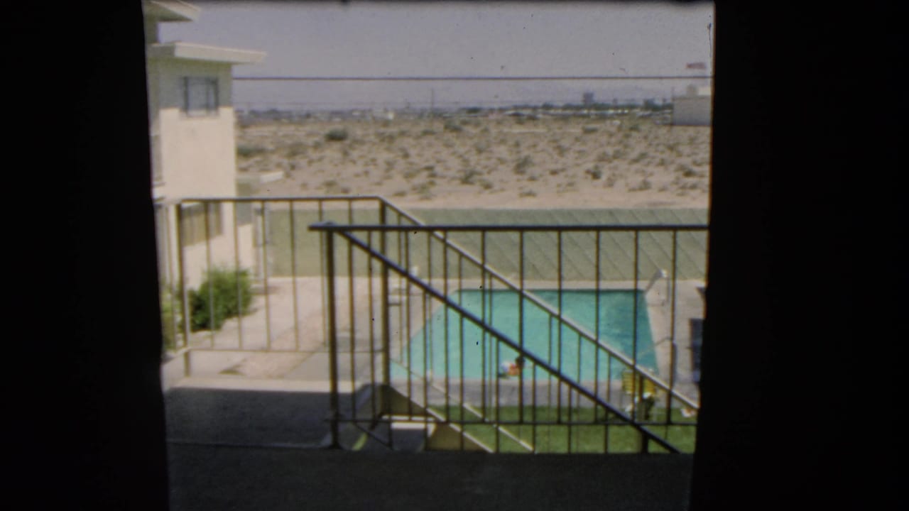 1966 Las Vegas home-movie frame looking past a balcony railing toward a swimmer in a private pool and desert beyond.